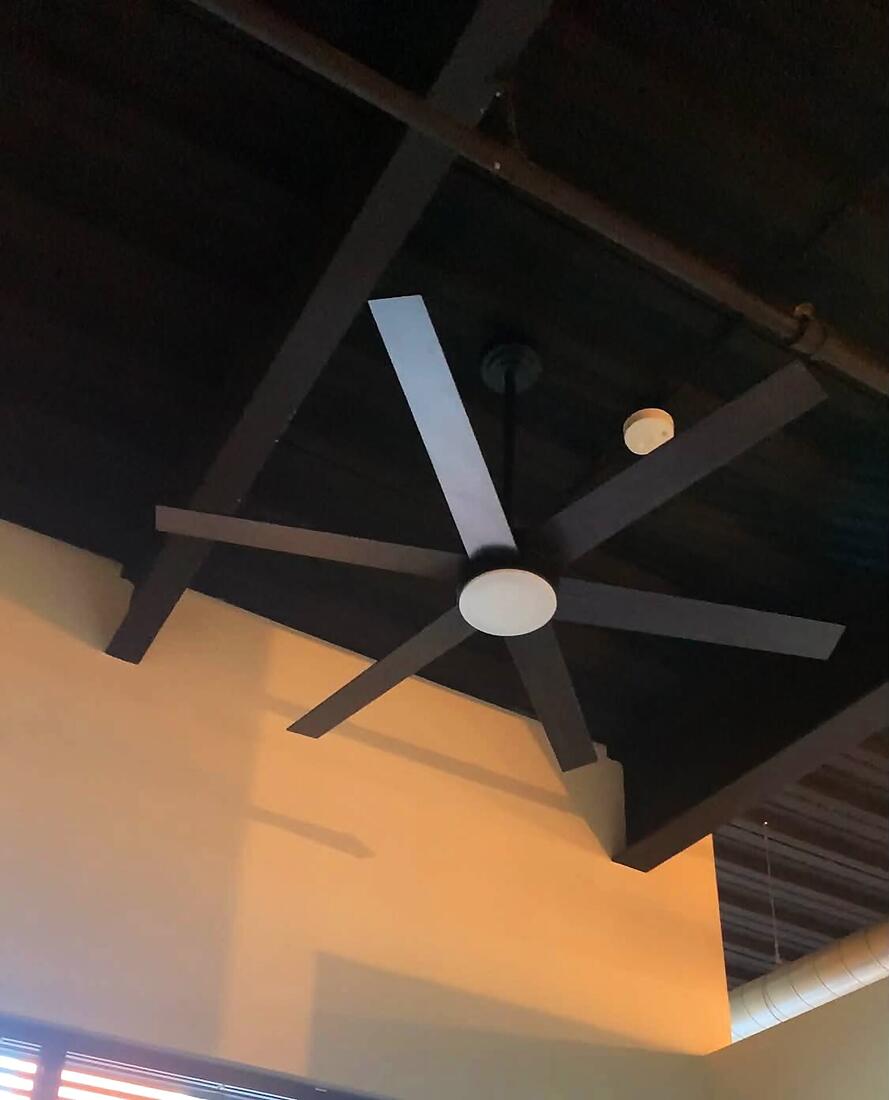 Black five-blade ceiling fan installed in a loft with exposed beams