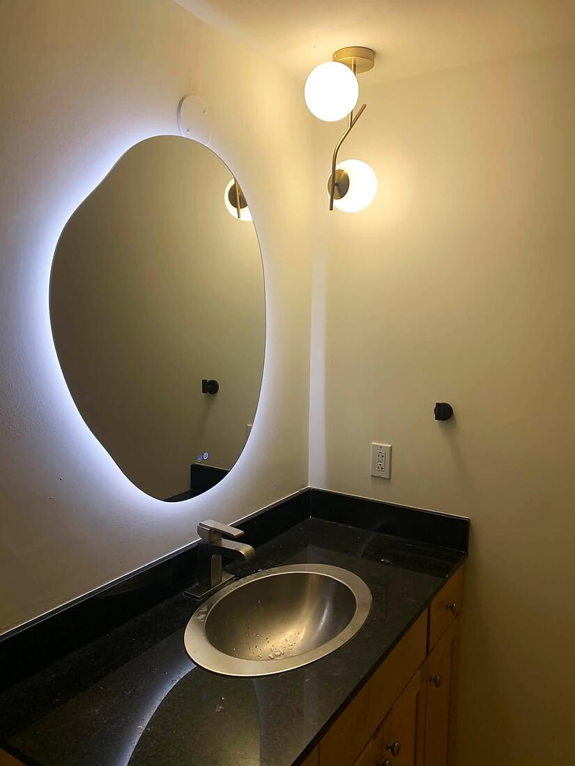 Backlit vanity mirror and globe wall sconces installed over a bathroom sink