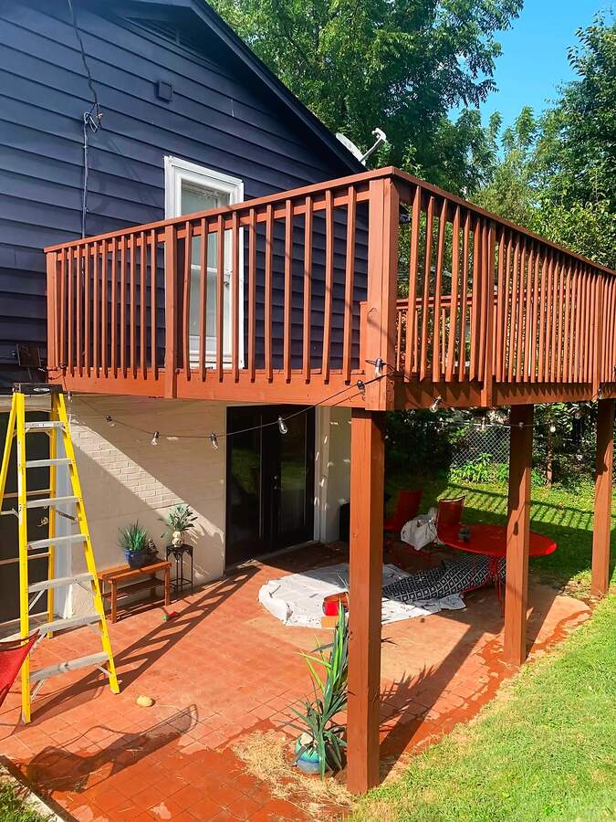 Stained wooden deck railings and posts above a backyard patio